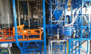 Vista angolare dell'impianto per la separazione di granuli di gomma con macchinari blu e ringhiere di sicurezza arancioni prodotto da Ghirarduzzi srl.
