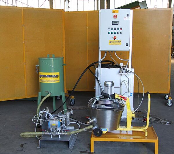 Release agent dispenser machine for ingot molds by Ghirarduzzi, used to apply release agents to ingot mold cakes to facilitate the detachment of freshly cast ingots. The structure consists of a control unit, a green tank, and a stainless steel component, located in an industrial area.