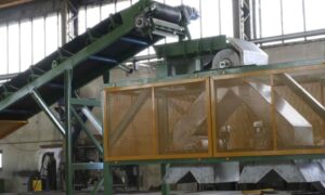 Sistema di separazione magnetica industriale con nastro trasportatore e tamburo magnetico, progettato per rimuovere materiali ferrosi durante i processi di riciclaggio e lavorazione.